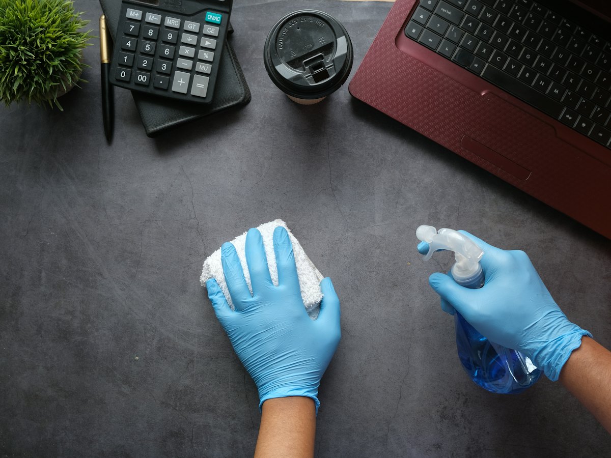 Manos con guantes limpiando una mesa de oficina